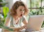 Une jeune femme assise à son bureau, devant son ordinateur portable, affiche une expression de choc avec la bouche grande ouverte et les yeux écarquillés.