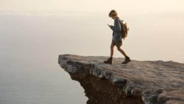 image générée d'un enfant qui discute avec un ami chatbot sur smartphone sans voir qu'il marche au bord d'une falaise