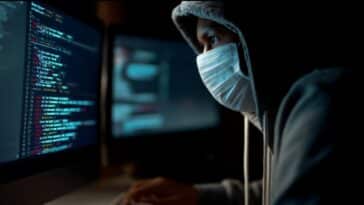 un homme en hoody et avec un masque chirurgical en train de rédiger des lignes de codes sur son ordinateur afin de perpétrer un scam en ligne à l'aide de l'IA