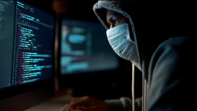 un homme en hoody et avec un masque chirurgical en train de rédiger des lignes de codes sur son ordinateur afin de perpétrer un scam en ligne à l'aide de l'IA