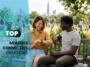 Un jeune couple assis sur un banc de parc consulte une montre connectée, avec des passants et la silhouette d'une ville à l'horizon.