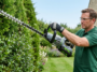 Un homme utilise le taille-haie à batterie EGO Power+ HT6510E pour entretenir une haie dense dans un jardin.