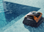 Le robot nettoyeur de piscine sans fil Beatbot Sora 30 orange et noir en train de se déplacer au fond de l'eau claire d'un bassin carrelé.