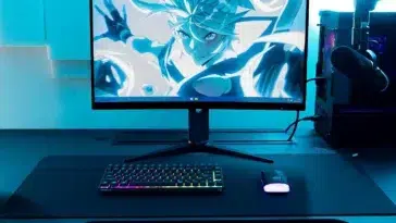 Vue d'ensemble d'une configuration de jeu éclairée en bleu avec un moniteur, un PC et un clavier CHERRY K33 compact.