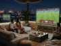 Amis installés sur une terrasse de toit en soirée devant le match de football Turquie vs Paraguay sur grand écran.