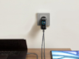 Un chargeur Anker Zolo 140W noir est branché dans une prise murale grise, alimentant simultanément un ordinateur portable et une tablette sur un bureau.