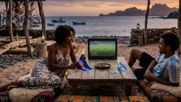 Un couple assis sur la plage regarde le match de football Argentine VS Cap Vert sur un petit écran au coucher du soleil