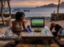 Un couple assis sur la plage regarde le match de football Argentine VS Cap Vert sur un petit écran au coucher du soleil