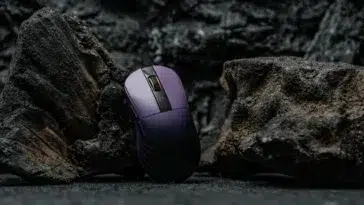 Souris gaming Epomaker Carbonis violette debout entre des rochers de lave noirs et texturés, éclairée de manière dramatique.
