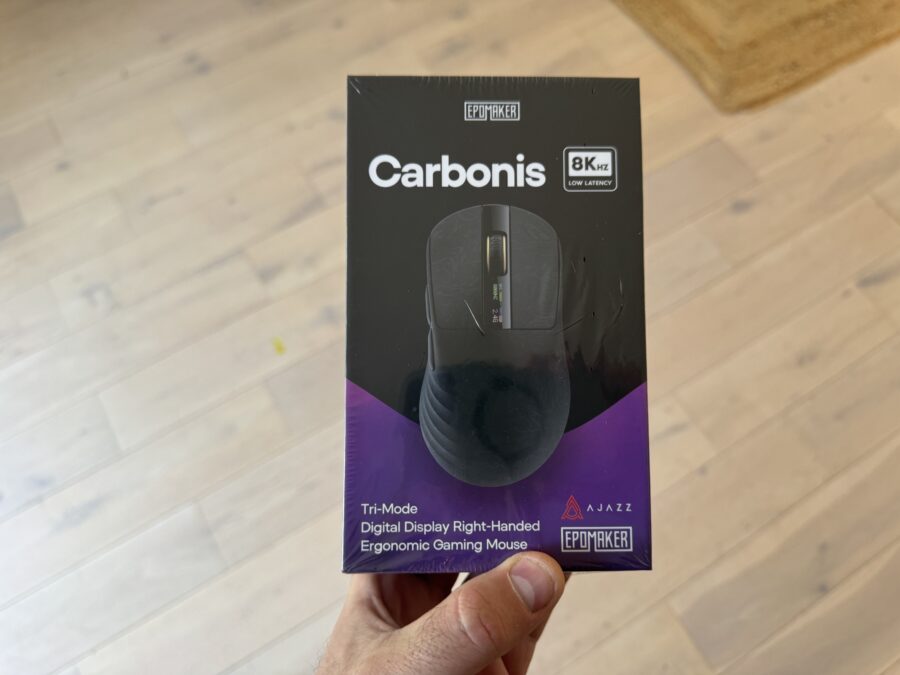 Une main tenant la boîte scellée de la souris gaming ergonomique Epomaker Carbonis, affichant les détails Tri-Mode et 8KHz.