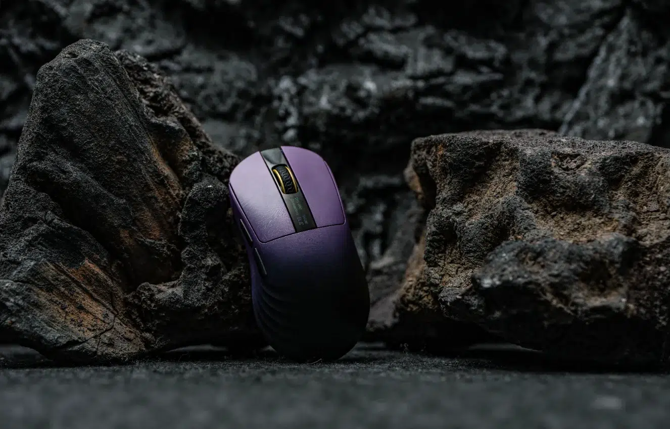 Souris gaming Epomaker Carbonis violette debout entre des rochers de lave noirs et texturés, éclairée de manière dramatique.