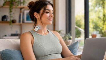 Une jeune femme souriante utilise son ordinateur portable tout en portant un petit climatiseur individuel Blö accroché à son col.