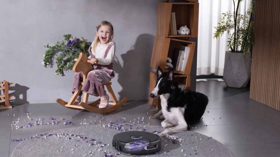Narwal Flow 2 en train de nettoyer des confettis sur un tapis près d'une enfant et d'un chien.