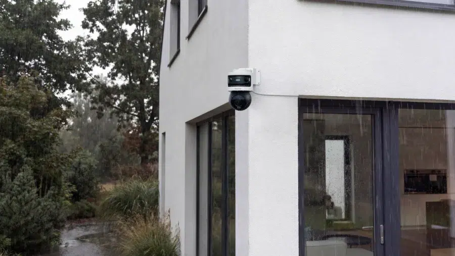 Une caméra OMVI 3i WiFi fonctionnant sous une forte pluie, montée sur le coin d'une maison moderne.