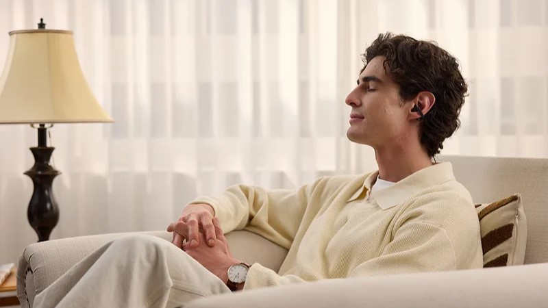 Homme assis dans son salon, détendu, écoutant de la musique avec les écouteurs Shokz OpenDots 2.