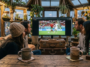 Groupe d'amis regardant un match de football entre la Suisse et l'Algérie sur un écran dans une véranda remplie de plantes
