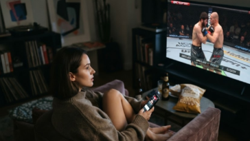 Femme regardant le combat UFC Fight Night Ankalaev vs Guskov à la télévision dans un salon cosy.