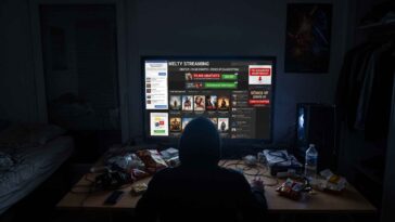 Un bureau désordonné avec un ordinateur affichant un site de streaming de films, entouré de snacks, de câbles et d'un poster.