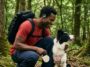 Un homme portant les écouteurs Shokz OpenFit Air 2, avec son chien en forêt, souriant à l'animal.