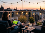 Personne regardant un match de football sur tablette depuis une terrasse en ville au coucher du soleil.
