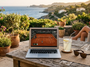 Ordinateur portable diffusant un match de tennis sur une terrasse méditerranéenne ensoleillée avec citronnade et lunettes de soleil.