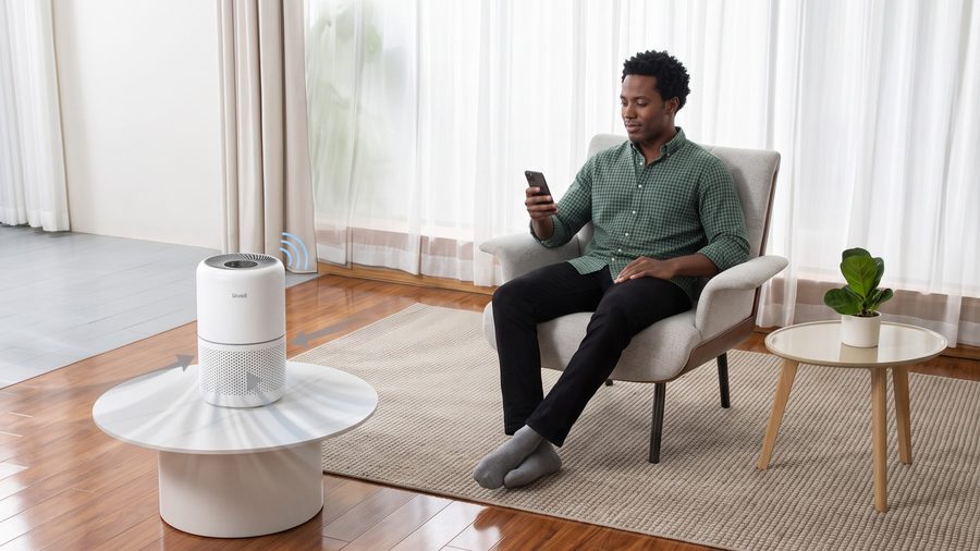 Un homme confortablement installé sur une chaise utilise son smartphone pour les fonctionnalités connectées du Levoit Core 300S Smart.